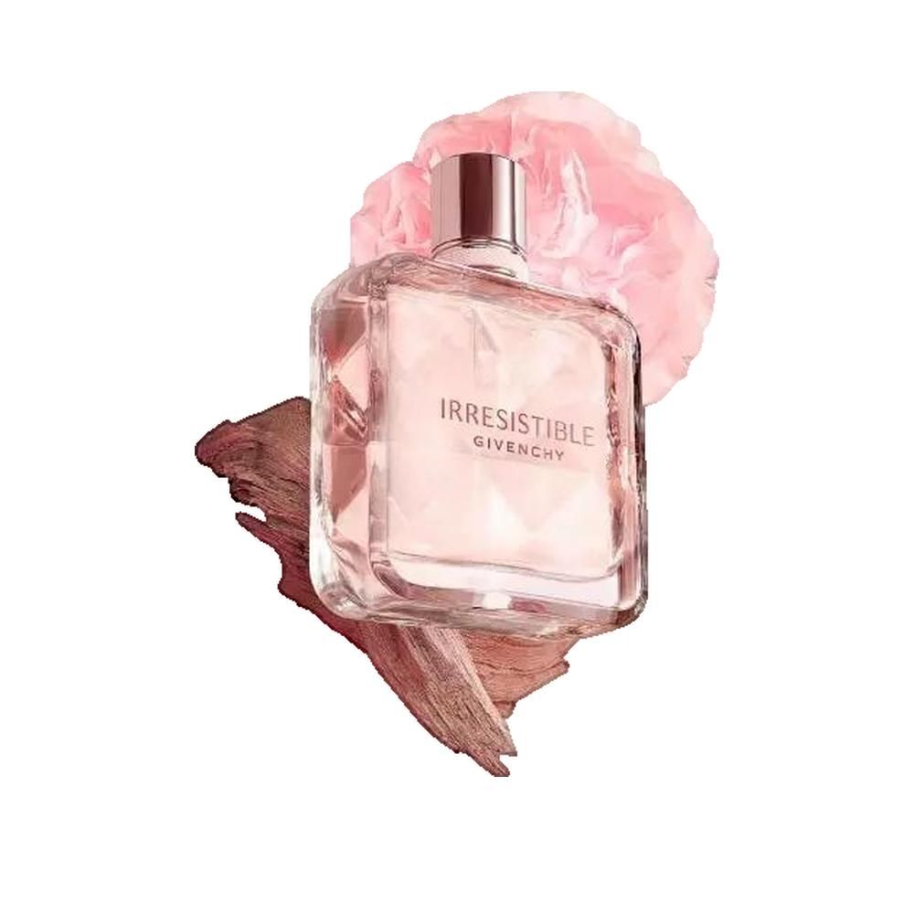 Flacone di profumo con contenuto rosa. Scritta: Irresistible Givenchy. Flacone quadrato con contenuto rosa. Con legno e fiore rosa.