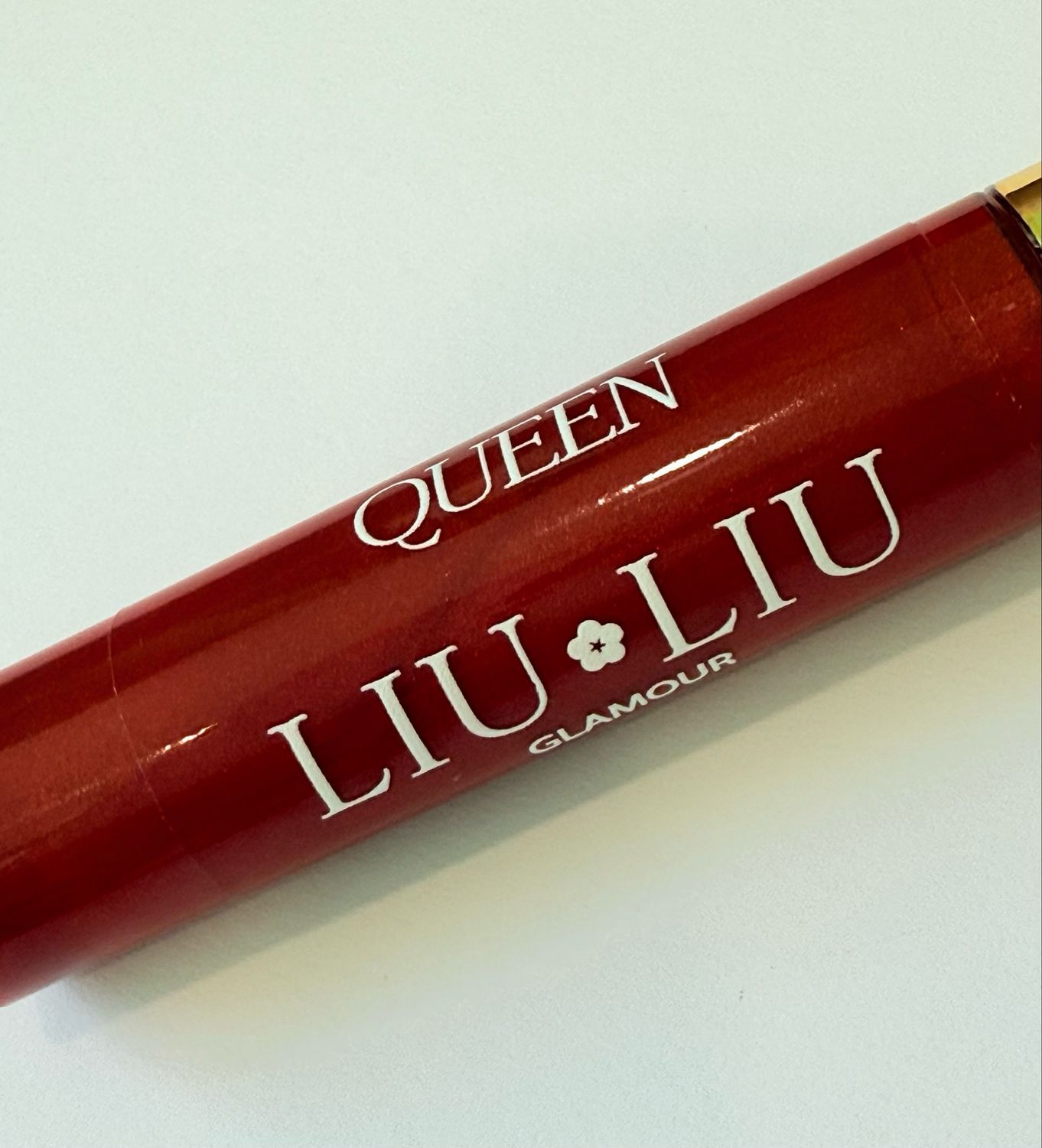 Primo piano del lucidalabbra rosso. Scritta: QUEEN LIU LIU Glamour. Prodotto in primo piano, in diagonale dall'alto.