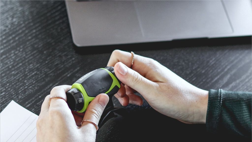 Mani che tengono un allenatore respiratorio. Dispositivo nero-verde. Sul dispositivo sono visibili dei numeri.