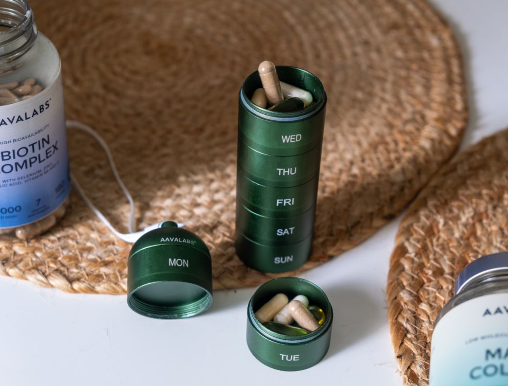 Portapillole verde a 7 scomparti, accanto a flaconi di pillole e scomparti aperti con pillole.