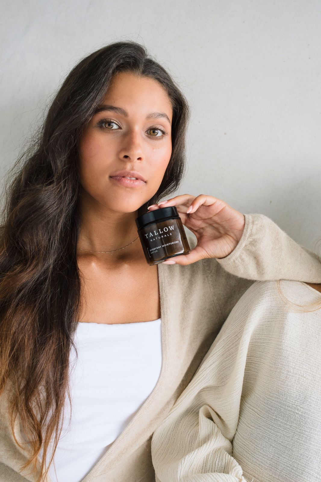 Donna che tiene un barattolo marrone con coperchio nero. Scritta: TALLOW NATURALS, BARRIER REPAIR LAVENDEL. Indossa un cardigan beige.