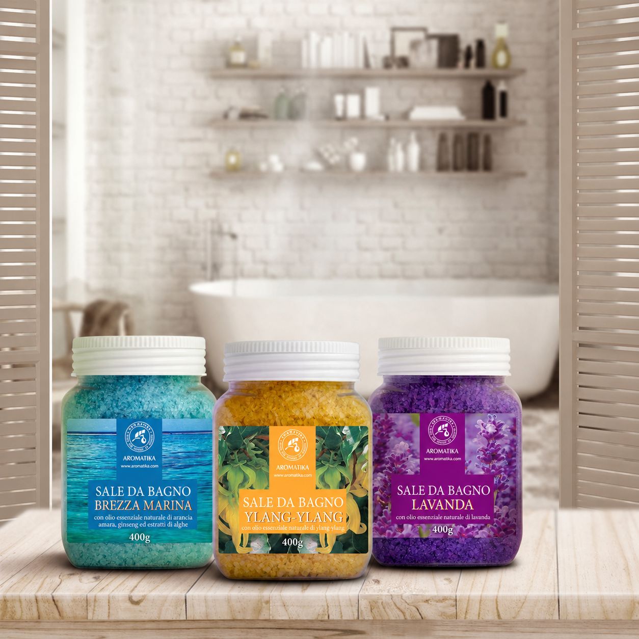 Tre barattoli di sali da bagno su un tavolo. Blu, giallo e viola. Scritte: Brezza Marina, Ylang-Ylang, Lavanda. Sfondo: bagno.