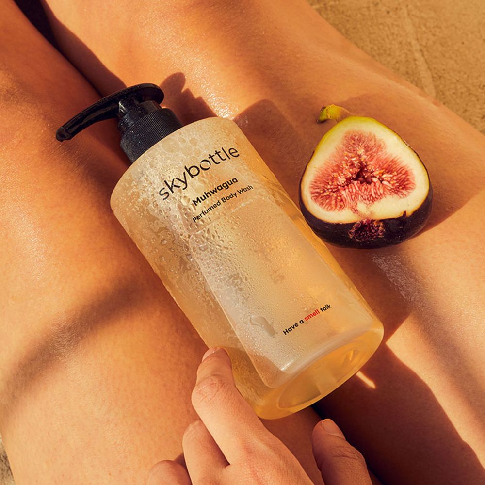 Flacone di gel doccia SKYBOTTLE Muhwagua su gambe. Accanto, un fico a metà.