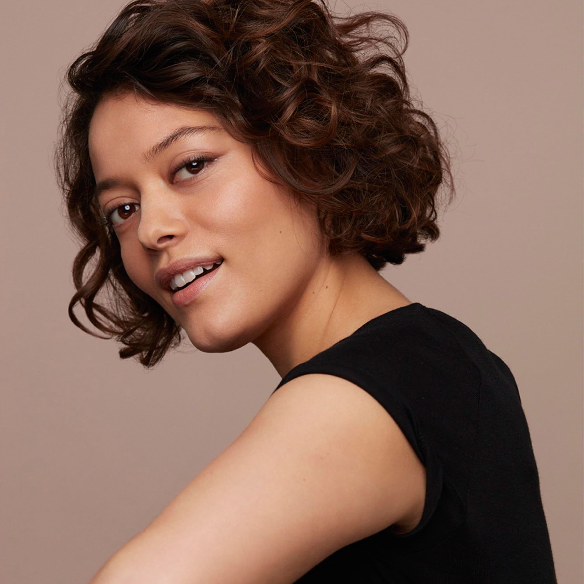 Ritratto di donna con capelli castani ricci. Indossa un top nero e sorride.