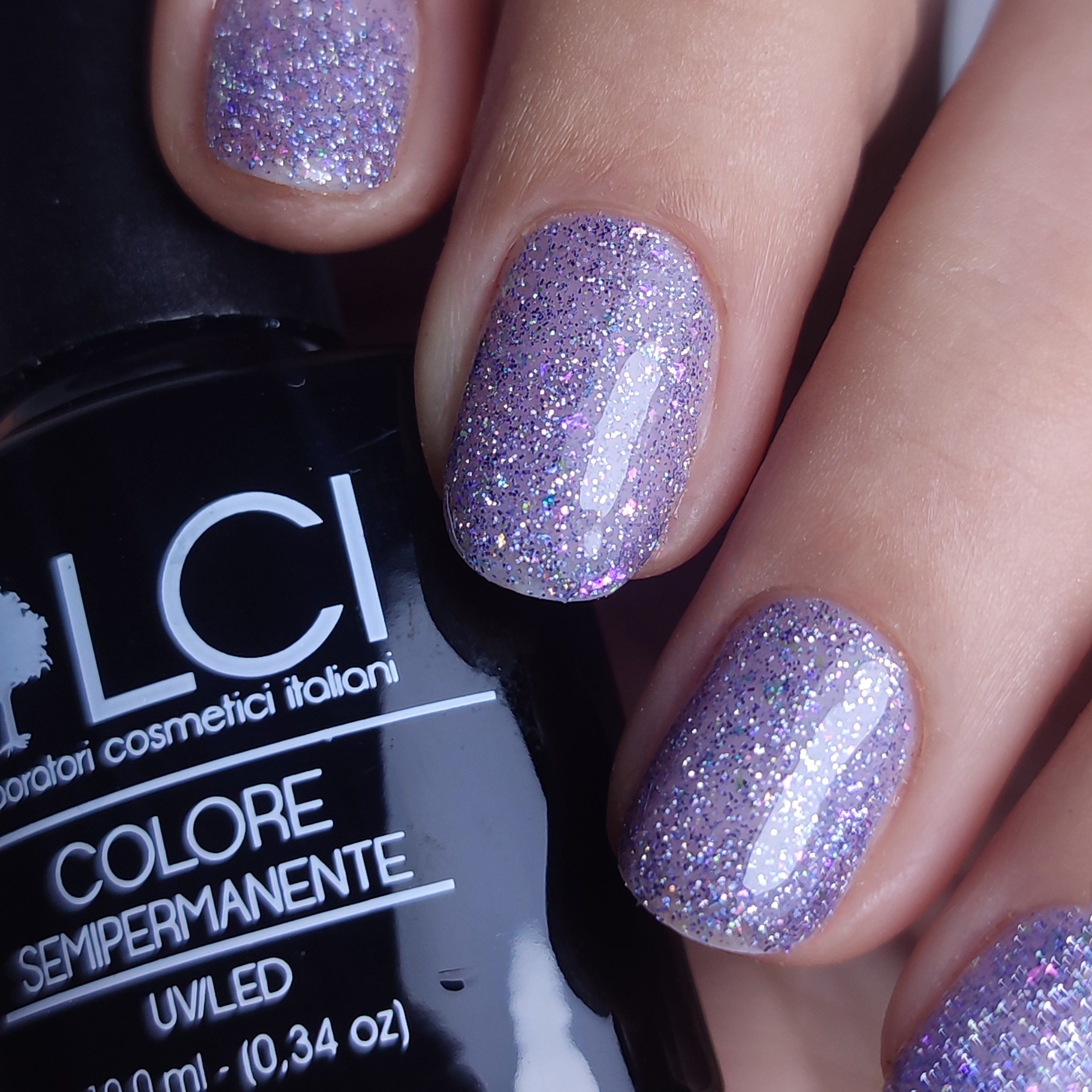 Unghie con smalto glitterato viola. Scritta: LCI, Colore Semipermanente, UVLED.