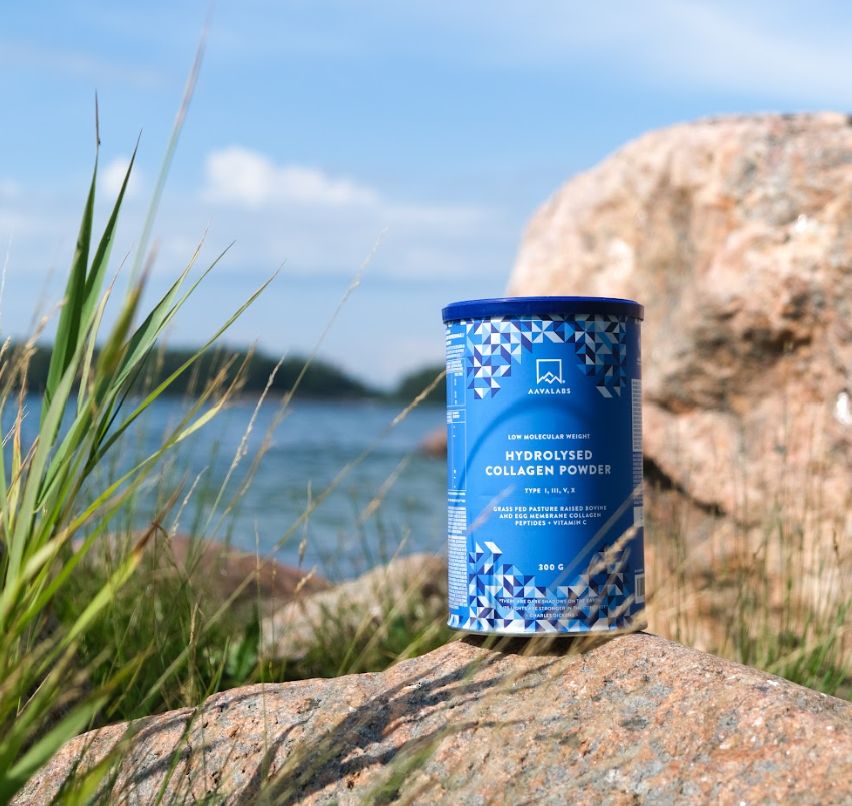 Barattolo blu di polvere di collagene su una roccia, acqua e cielo sullo sfondo. Nome del prodotto visibile.