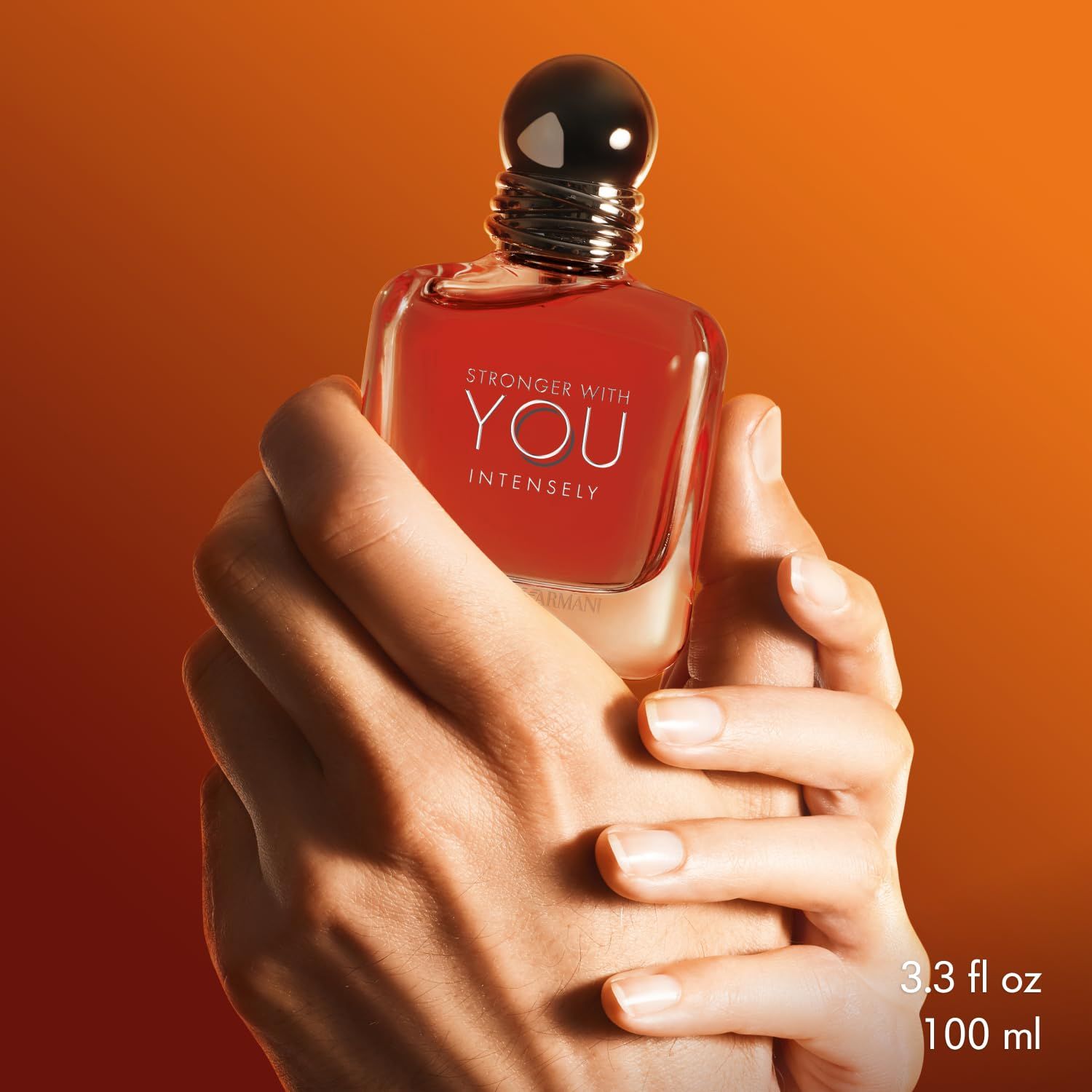Flacone in vetro con liquido rosso, tenuto in mano. Scritta: Stronger With You Intensely. Testo: 3.3 fl oz 100 ml.