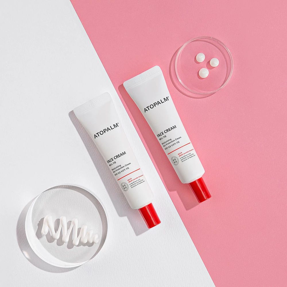 Due tubi con tappo rosso. Scritta ATOPALM FACE CREAM. Su sfondo rosa e bianco.