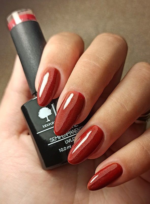 Mano con unghie smaltate e flacone di smalto. Colore: rosso. Scritta: LCI, COLORE SEMIPERMANENTE.