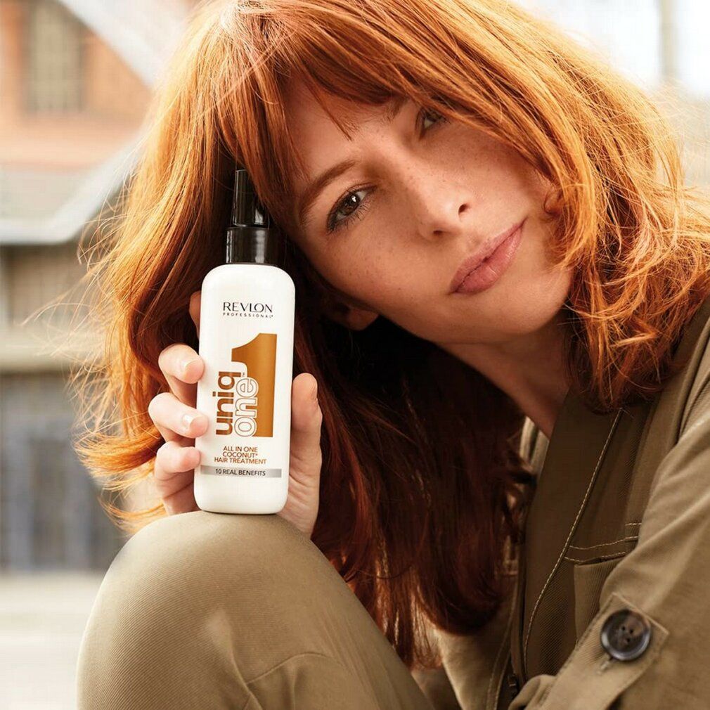 Donna tiene uno spray bianco con erogatore nero. Scritta: Revlon Professional Uniq One Coconut Hair Treatment.