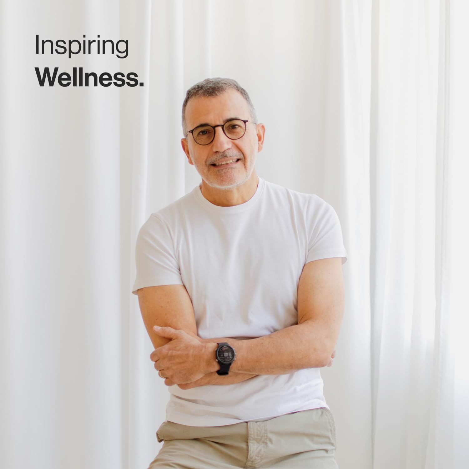 Un uomo con occhiali e orologio sorride alla telecamera. Indossa una maglietta bianca.