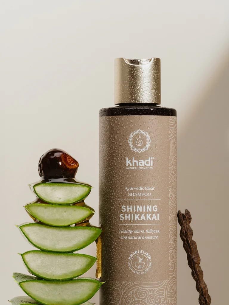 Flacone di shampoo Khadi Shining Shikakai con tappo. Accanto ad aloe vera e un pezzo di legno. Testo: Elisir ayurvedico, idratazione naturale.