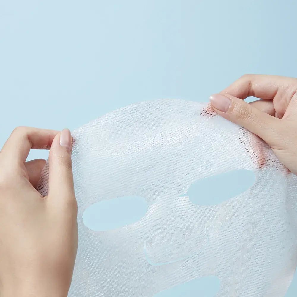 Maschera facciale in tessuto bianco, tenuta da due mani. Fori per occhi, naso e bocca visibili.