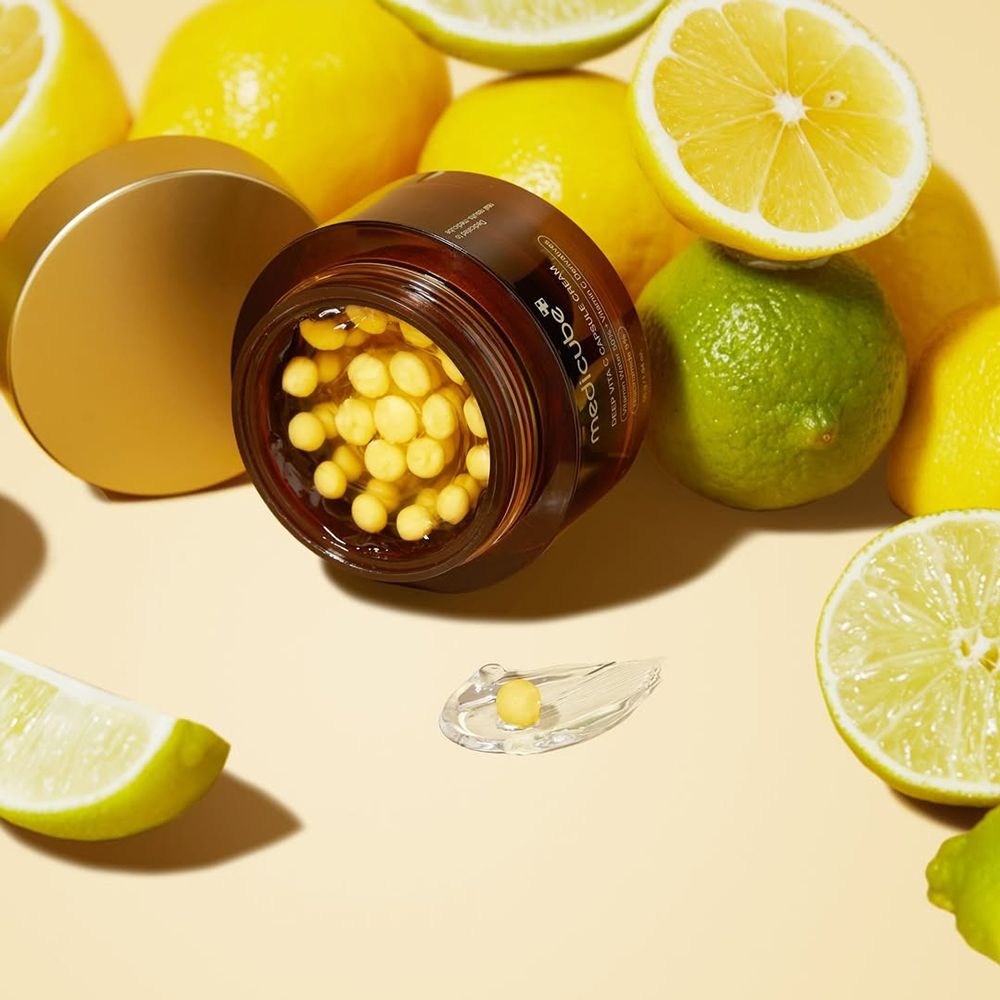 Prodotto con coperchio aperto, capsule gialle. Limoni e lime sullo sfondo.