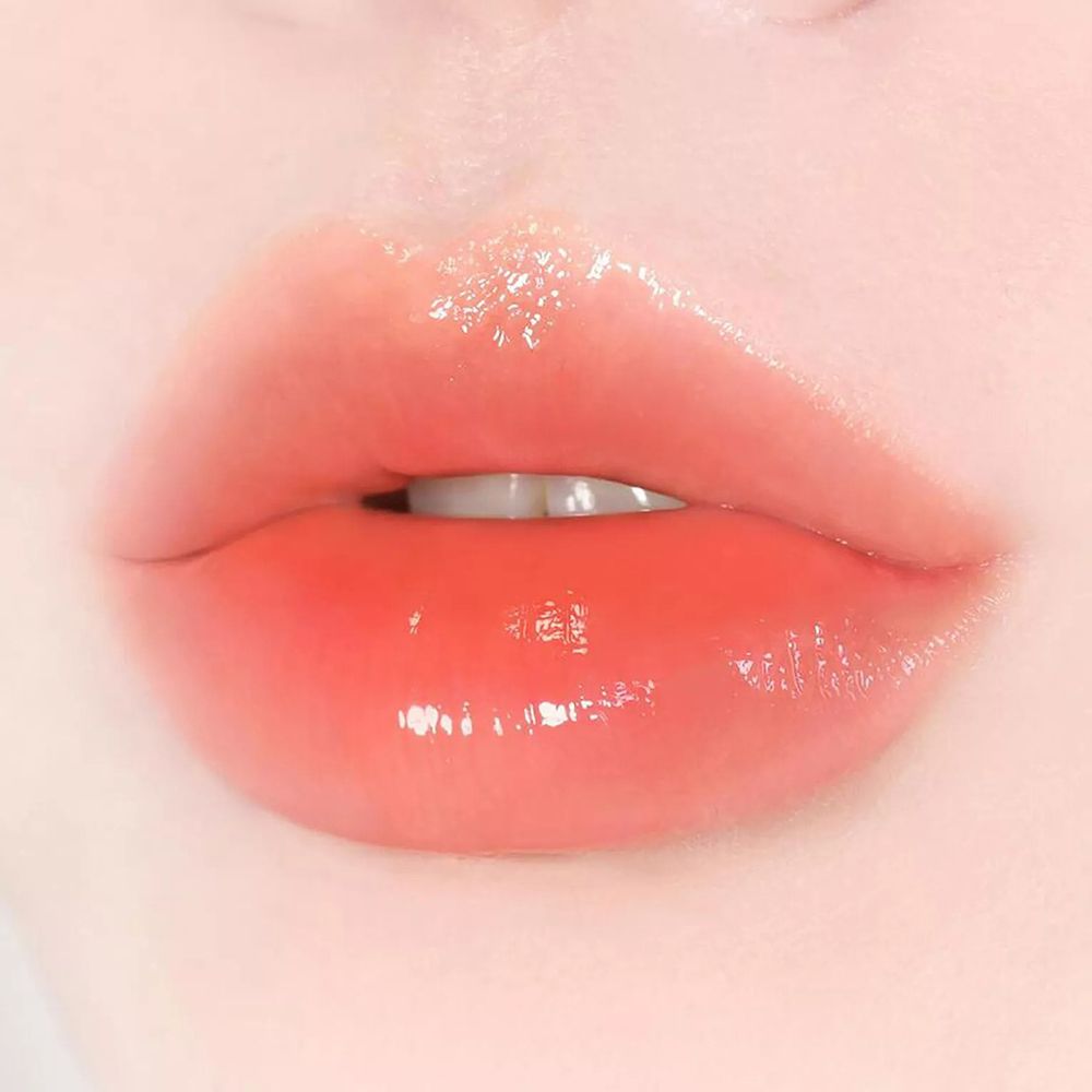 Primo piano di labbra con balsamo labbra lucido e arancione. Le labbra sono leggermente aperte.