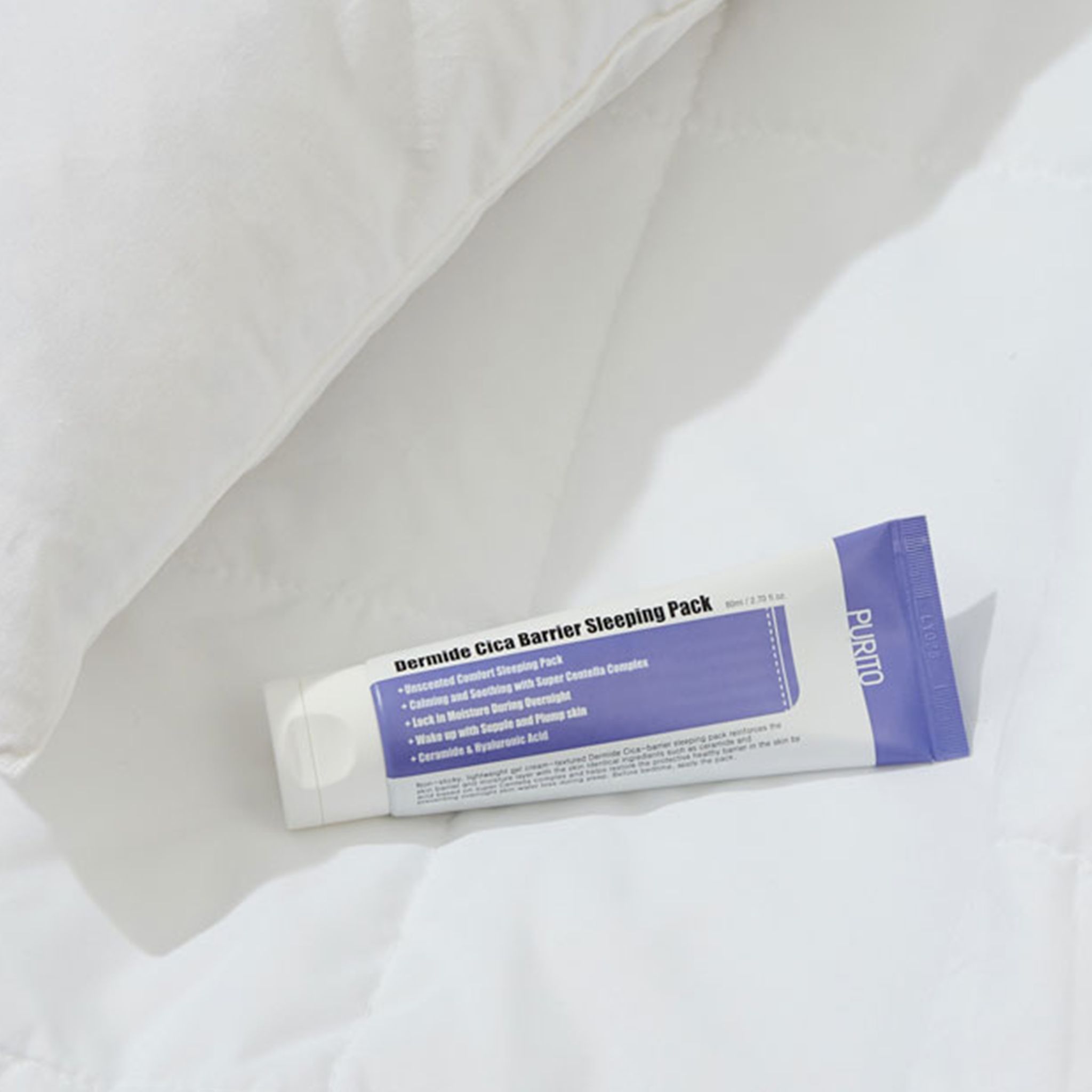 Prodotto su biancheria da letto bianca. Tubo con nome del prodotto e ingredienti. Marchio PURITO. Testo: Dermide Cica Barrier Sleeping Pack.