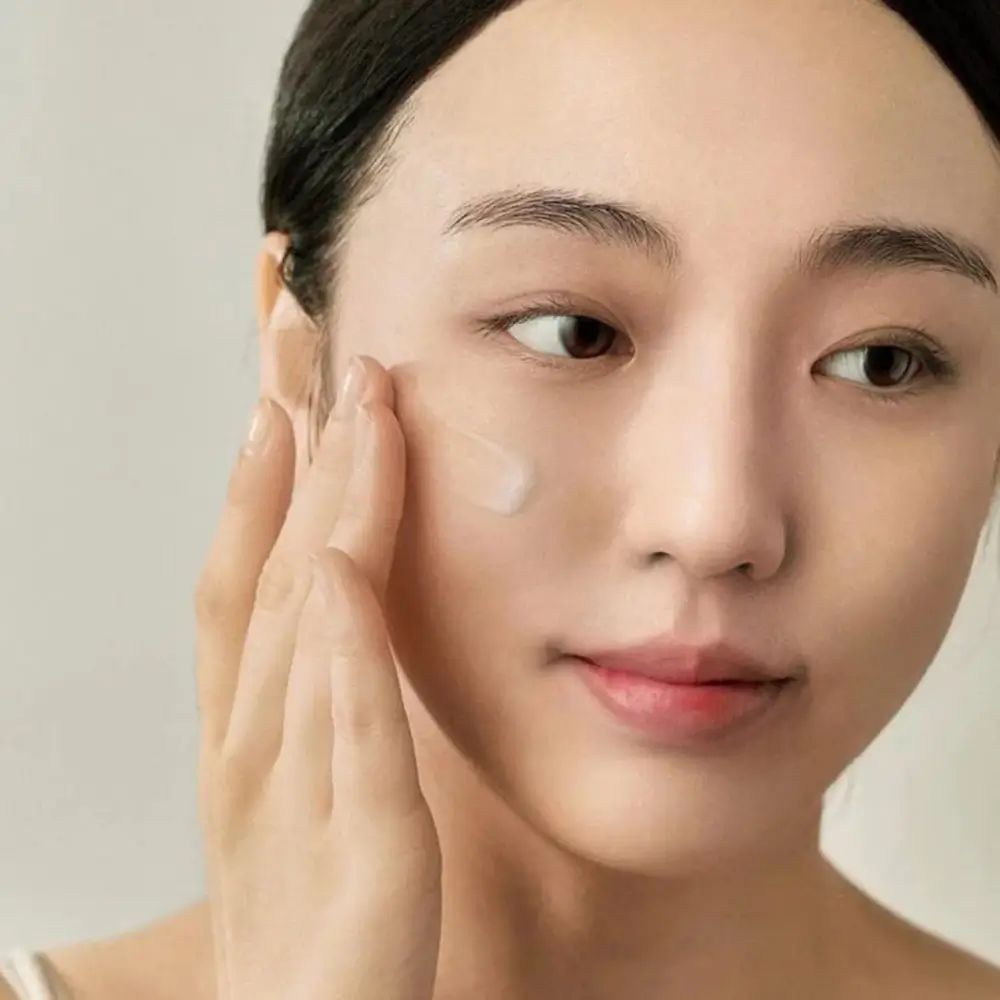 Donna applica il prodotto. Prodotto: Light on Serum. Donna con occhi chiusi. Sfondo: chiaro.