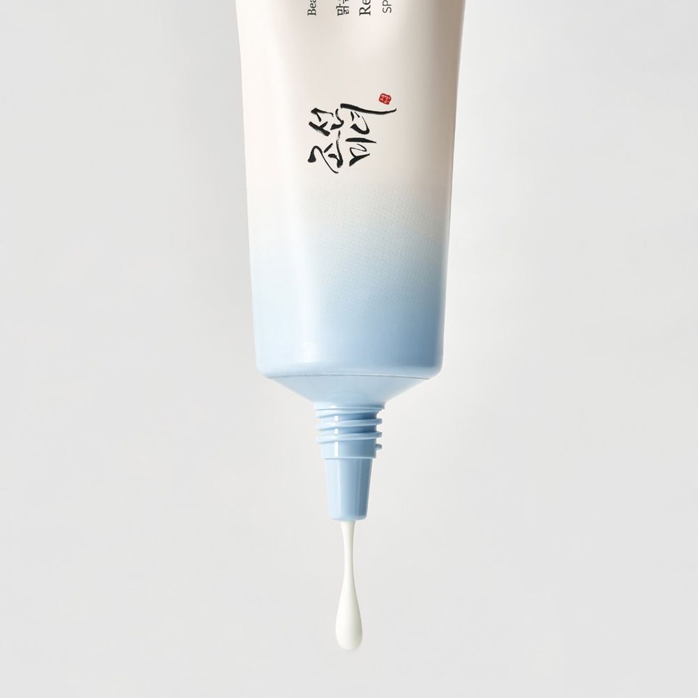 Tubo da cui gocciola crema. Tappo blu. Sfondo bianco.