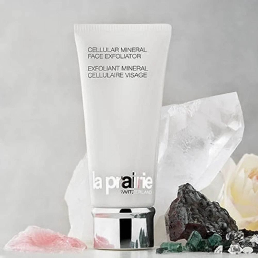Tubo bianco con testo e logo del prodotto. Circondato da pietre e fiori. Marchio: La Prairie.
