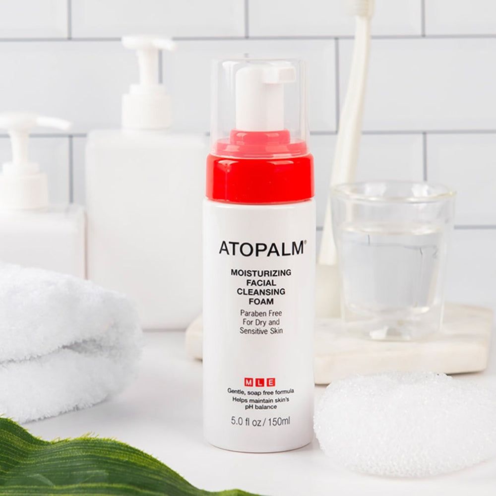 Flacone bianco con tappo rosso. Scritta: ATOPALM, schiuma detergente idratante. Contesto bagno.
