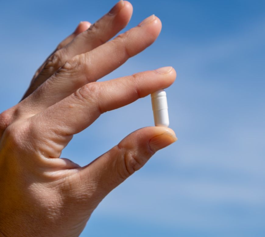 Mano che tiene una capsula di citrato di magnesio davanti al cielo blu.