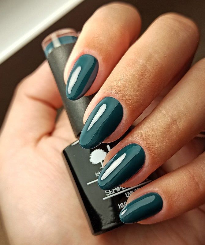 Mano che tiene un flacone di smalto verde scuro. Unghie smaltate dello stesso colore.