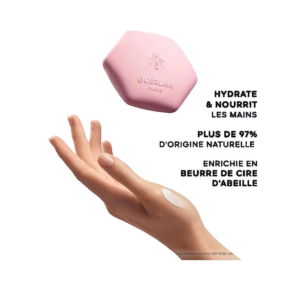 Contenitore rosa esagonale di crema mani Rosa Rossa, con ape e scritta Guerlain. Mano con crema.