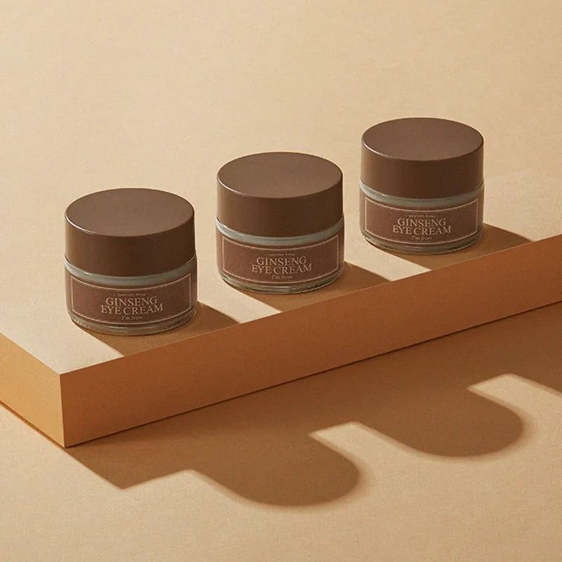 Tre vasetti di crema per occhi con coperchi marroni. Testo: Ginseng Eye Cream, I'm from. Su piedistallo.