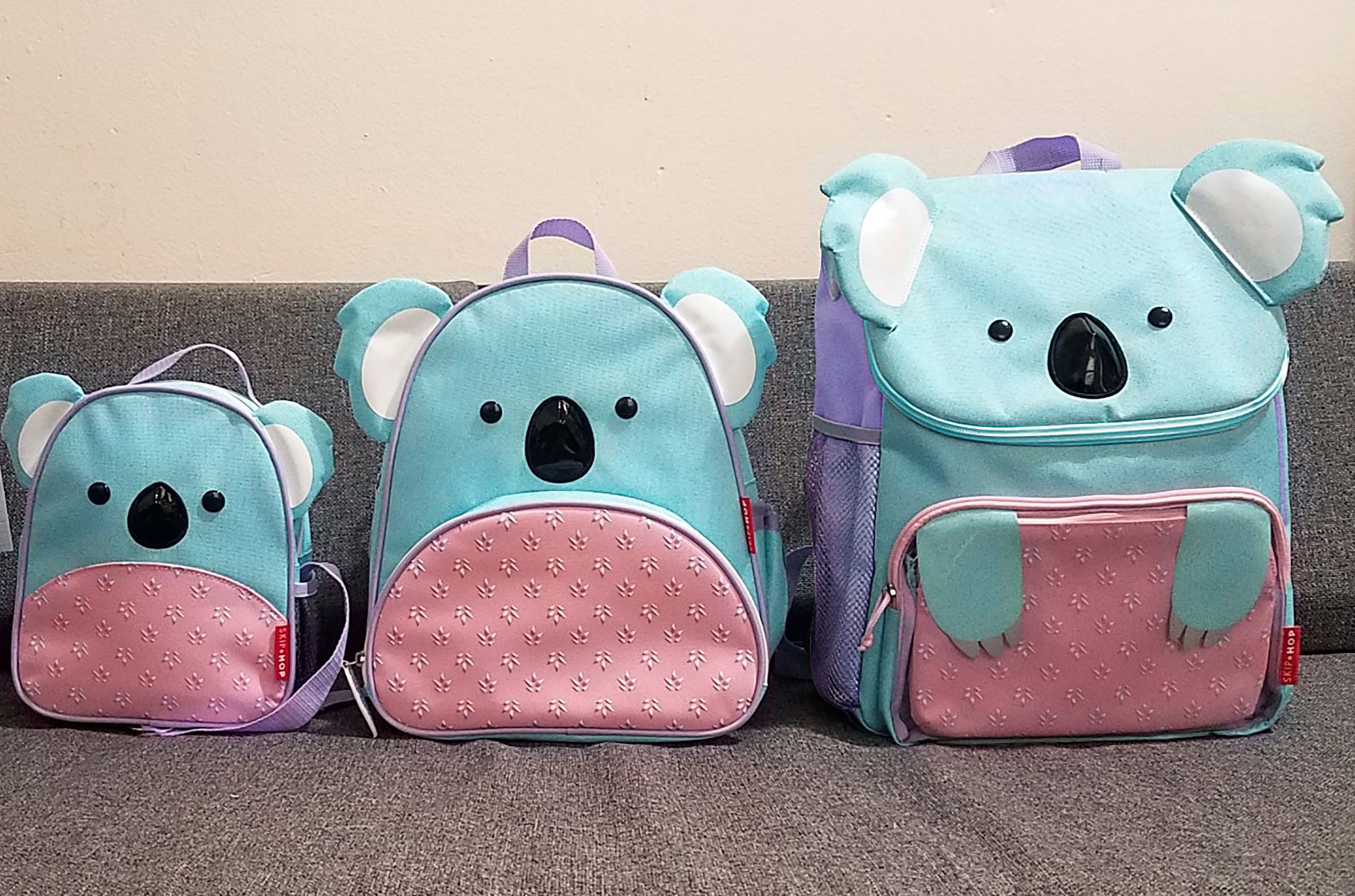 Tre zaini Skip Hop Zoo Koala. Diverse dimensioni. Blu e rosa. Su divano grigio.