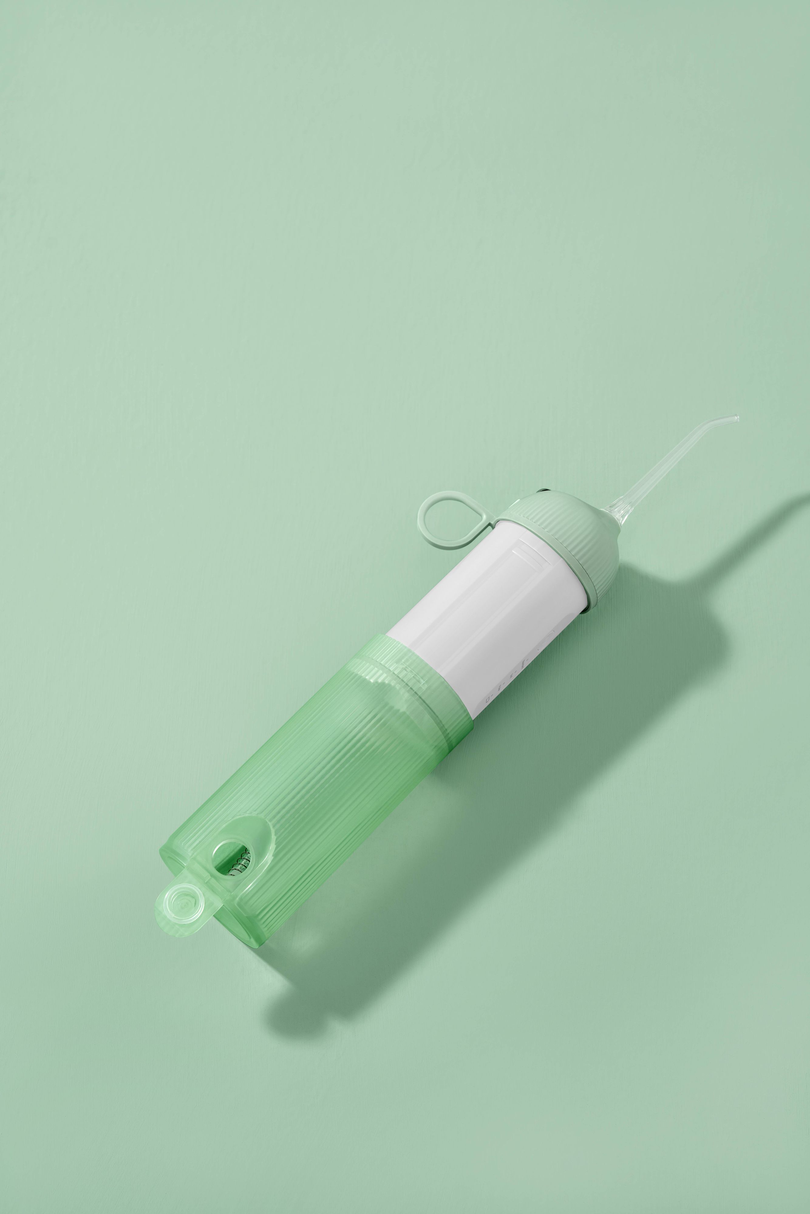 Idropulsore verde, parzialmente smontato. Corpo cilindrico, parte centrale bianca. Su sfondo verde.