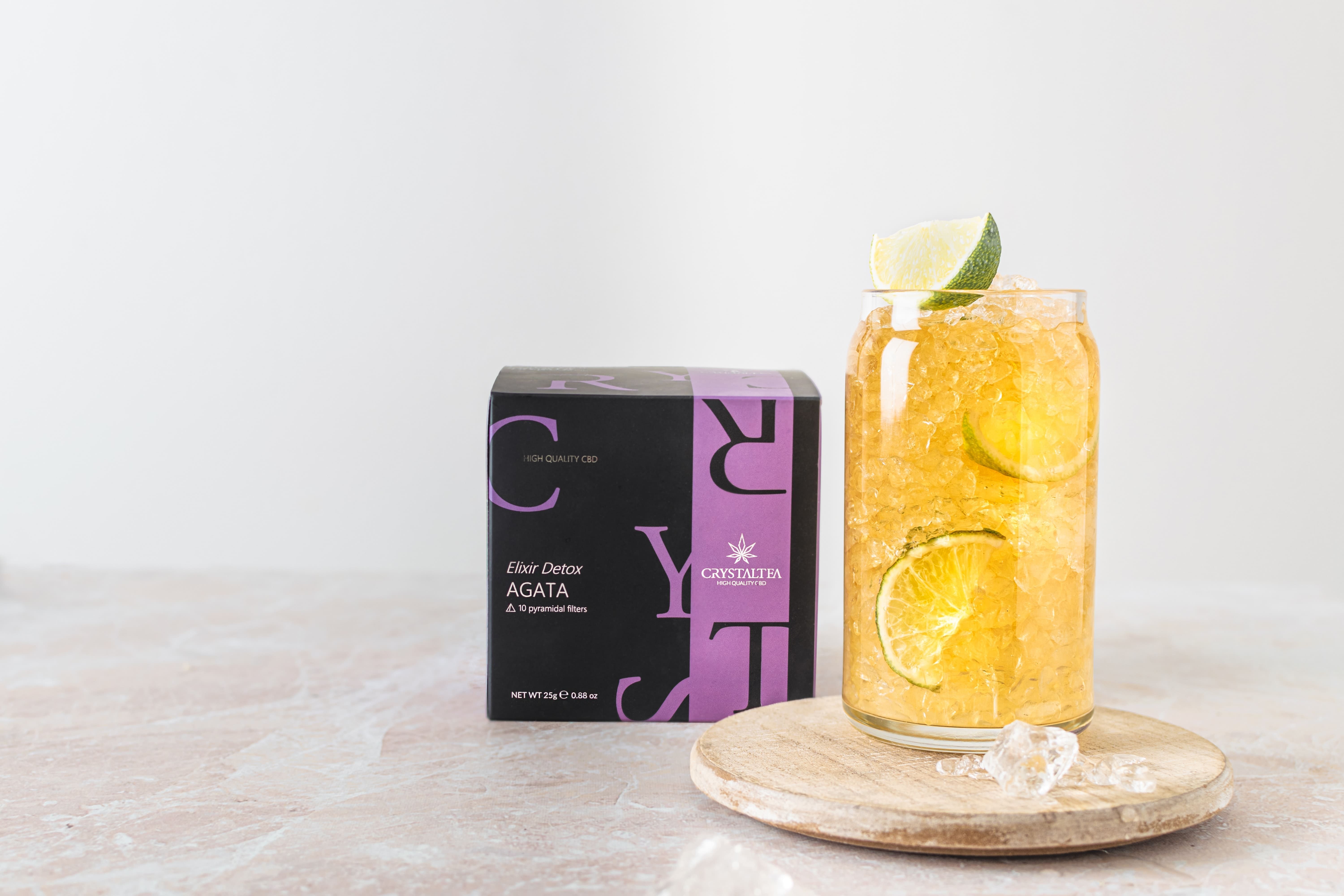 Bicchiere con bevanda, fette di lime e cubetti di ghiaccio. Accanto, una scatola con informazioni sul prodotto.