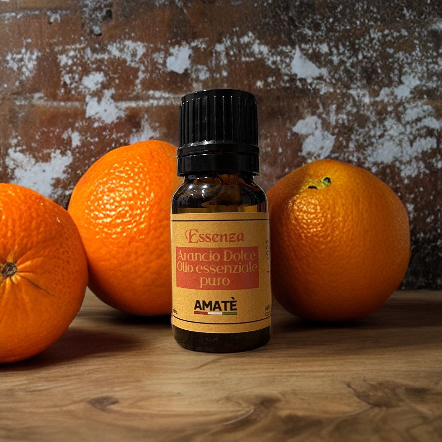Flacone di vetro marrone con tappo nero, accanto ad arance. Etichetta con testo: Arancio Dolce, Olio essenziale puro, AMATÈ.