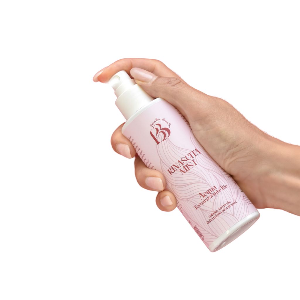 Mano che tiene flacone rosa con vaporizzatore. Scritta: Rinascita Mist, Acqua Texturizzante Bio. Logo: B.
