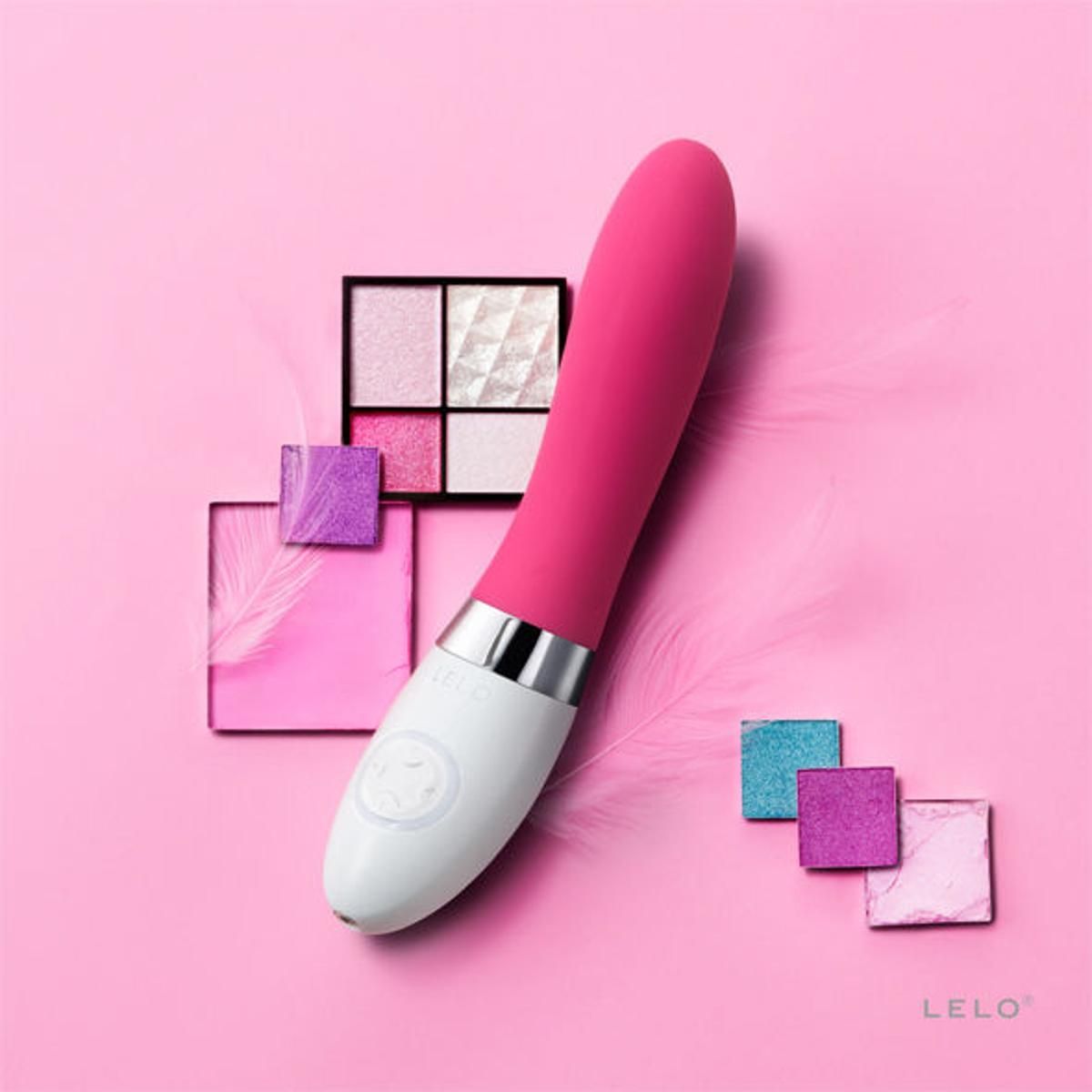 Vibratore rosa e bianco con prodotti cosmetici su sfondo rosa. Il logo del marchio LELO è visibile.