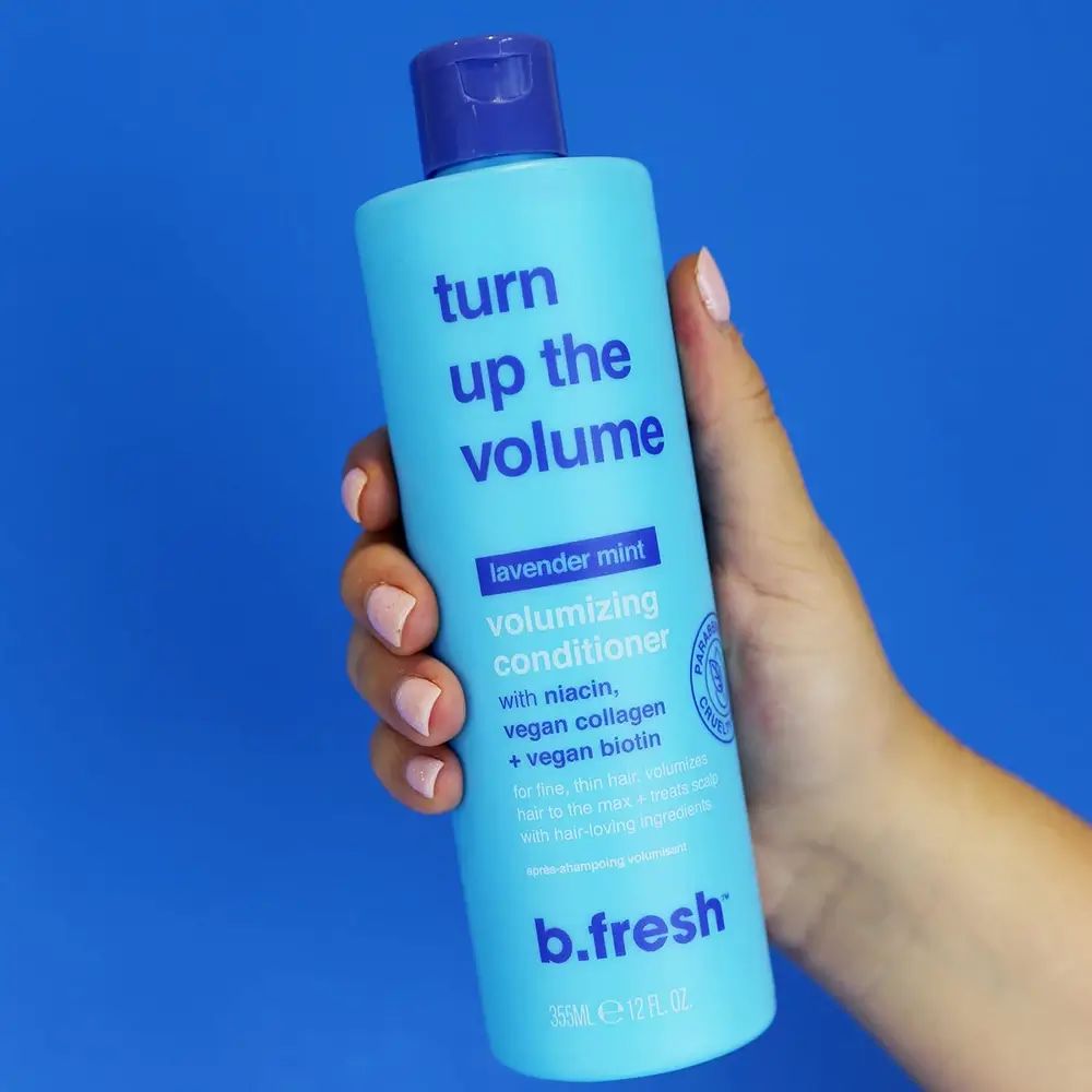 Shampoo azzurro con tappo blu. Scritta: Turn up the volume, volumizing conditioner. Marchio: b.fresh. Mano che tiene la bottiglia.