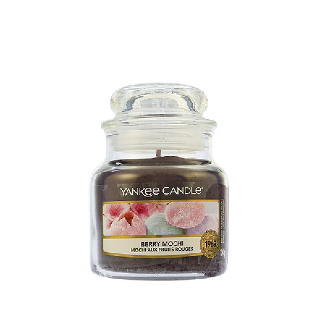 Piccola candela profumata in vaso con coperchio. Etichetta con nome prodotto e immagine mochi. Cornice dorata, marchio qualità.