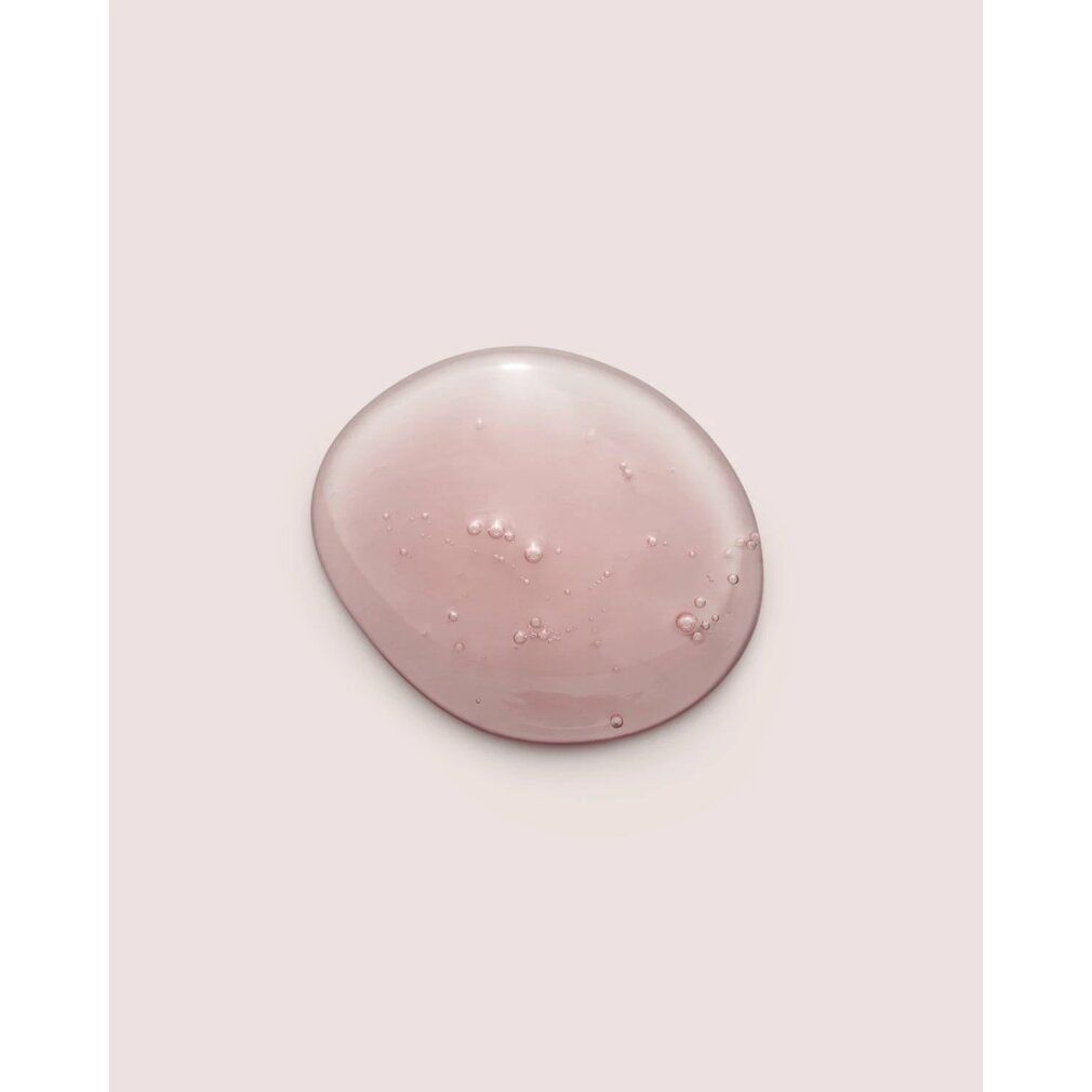 Goccia di shampoo trasparente e rosa con piccole bolle. Su sfondo rosa.