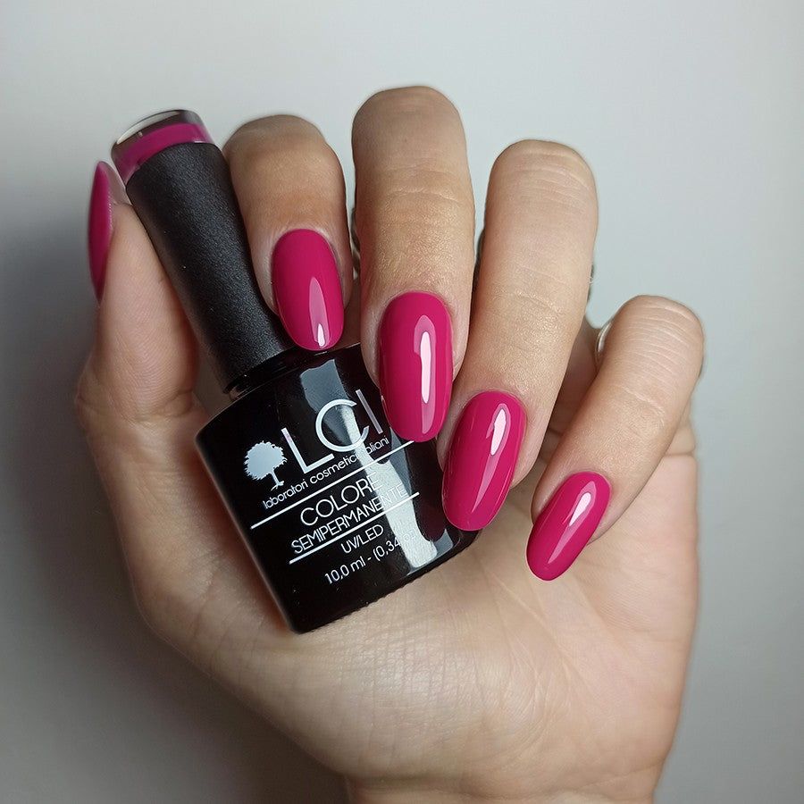 Mano con unghie smaltate e flacone di smalto. Unghie smaltate di rosso. Flacone di smalto nero con testo bianco.