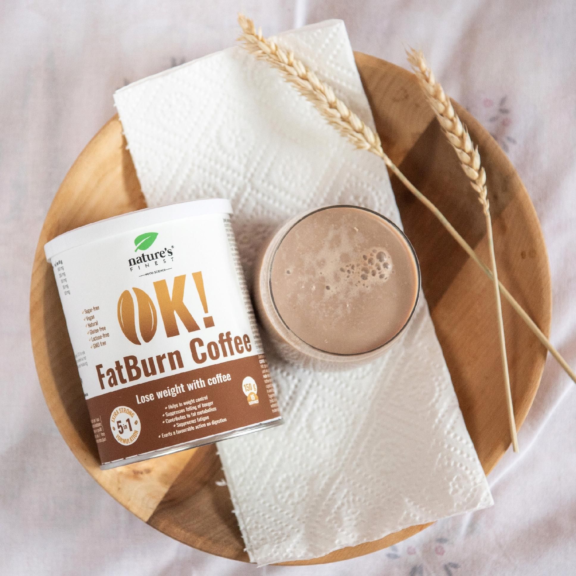 Lattina OK! FatBurn Coffee accanto a una tazza di caffè su un piatto di legno.