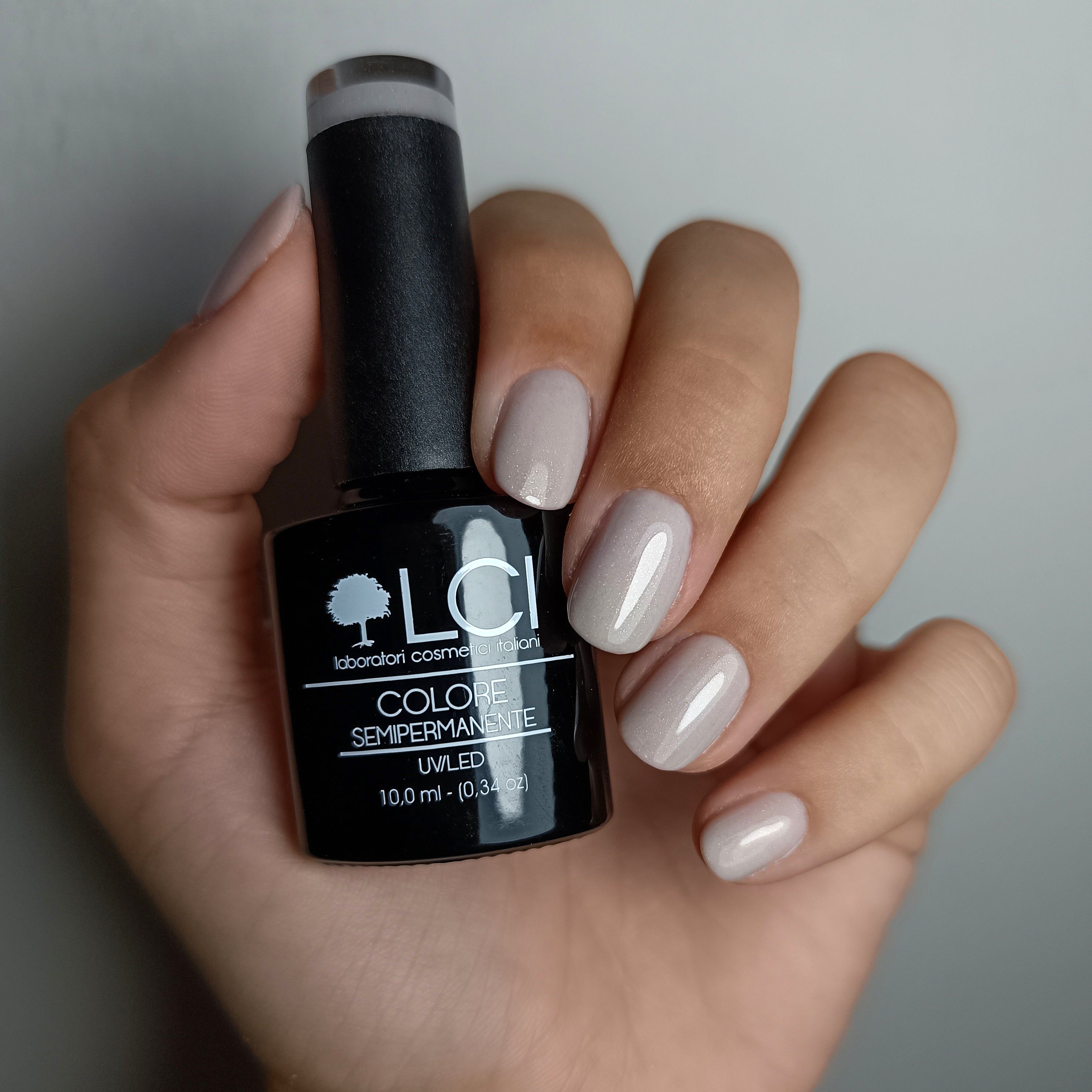 Mano con unghie smaltate e flacone di smalto. Unghie smaltate di grigio. Flacone con logo e testo.