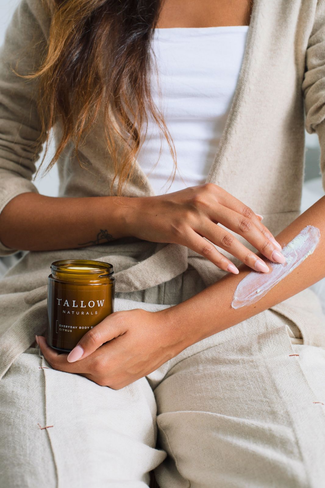 Donna applica burro corpo sul braccio. Barattolo marrone con coperchio nero. Scritta: TALLOW NATURALS, EVERYDAY BODY BUTTER CITRUS.