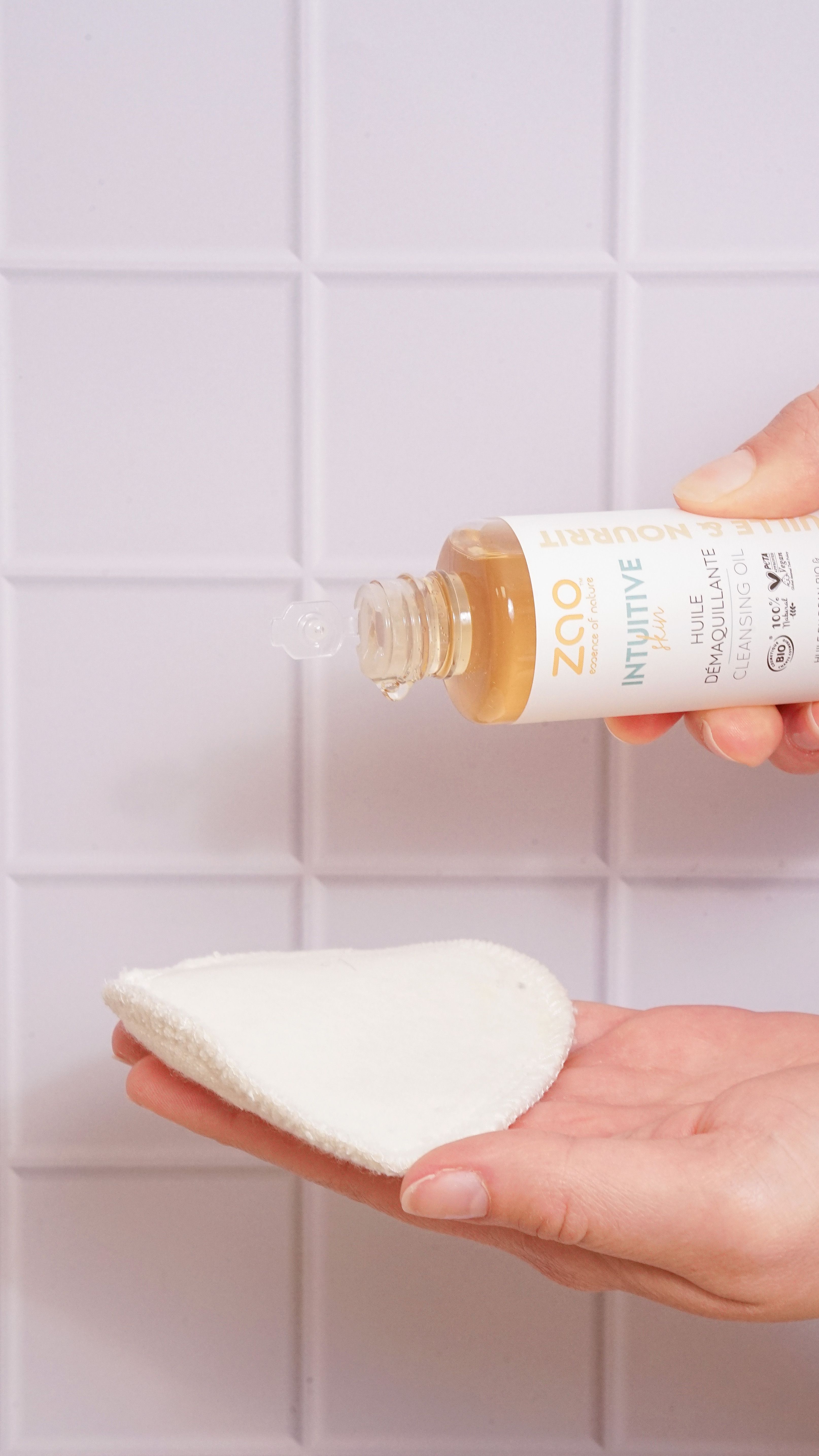 Liquido chiaro versato da una bottiglia su un dischetto. Bottiglia con tappo in legno, etichetta con testo. Sfondo: piastrelle bianche.