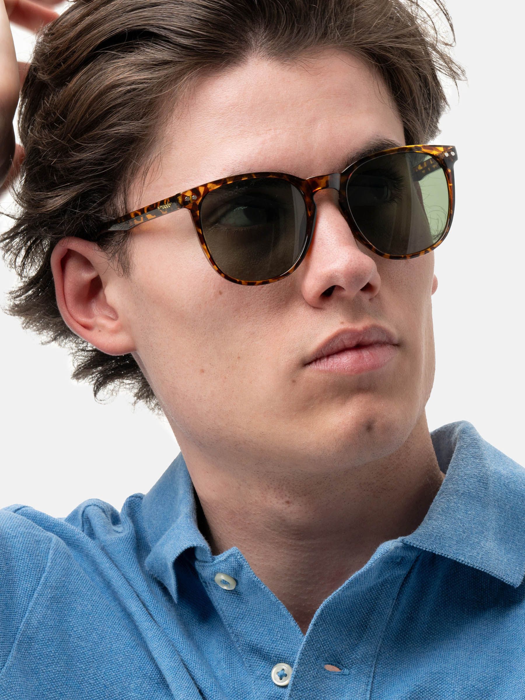 Uomo con occhiali da sole marroni con motivo tartarugato e lenti verdi. Il nome del marchio "smooder" è visibile.