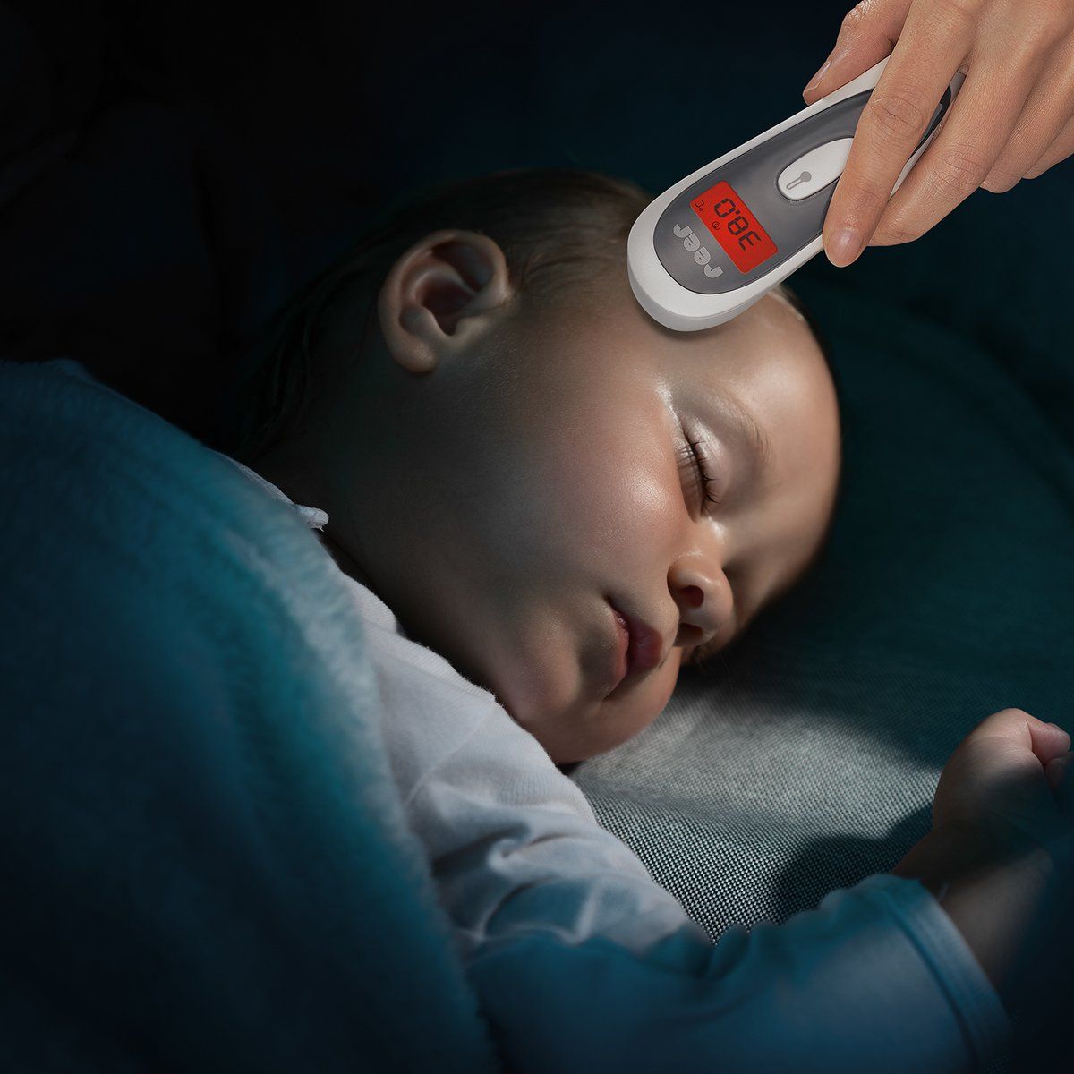 Mano che tiene un termometro a infrarossi senza contatto sulla fronte di un bambino che dorme. Display: 38,0 °C.