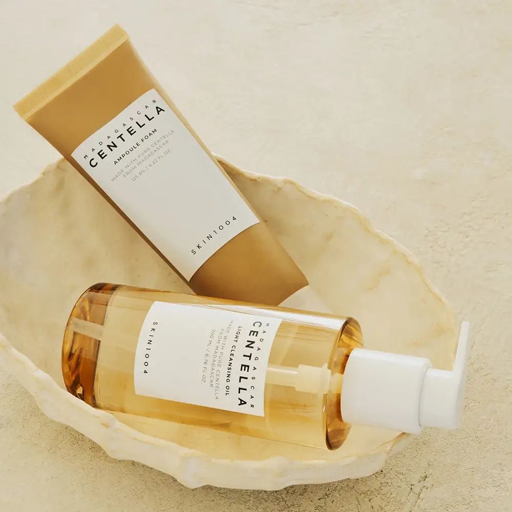 Due prodotti in una conchiglia. A sinistra, un tubetto, a destra, una bottiglia con pompa. Entrambi con etichette.