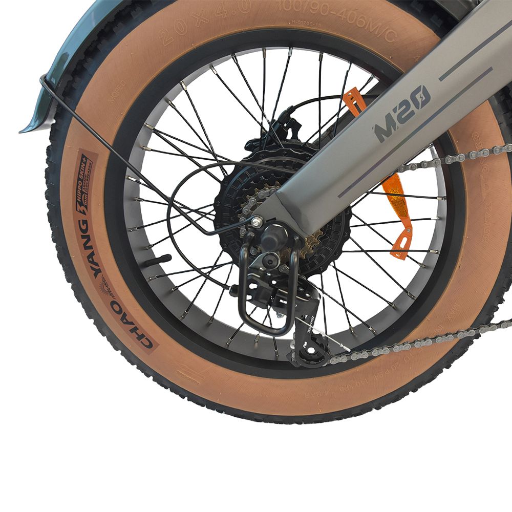 Primo piano della ruota posteriore di una dirt bike elettrica grigia. Pneumatico marrone, catena nera e dettagli. Scritta 'M20'.