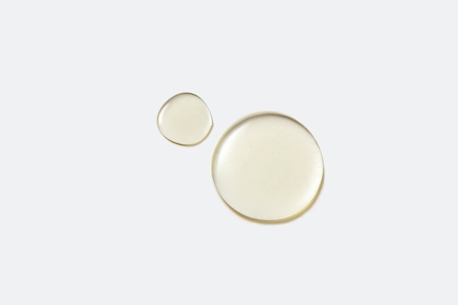 Due gocce di liquido giallo chiaro su sfondo bianco. Una piccola e una grande goccia.