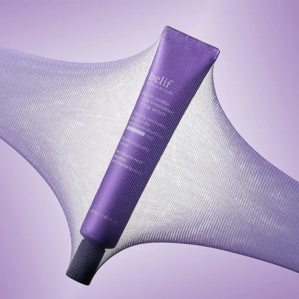 Tubo di crema contorno occhi Belif su tessuto viola. Il tessuto è elastico e trasparente.