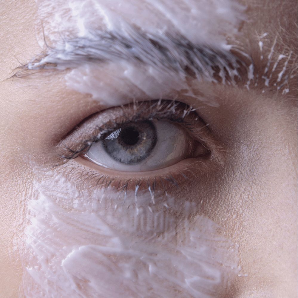 Primo piano di un occhio con crema bianca su sopracciglia e pelle.