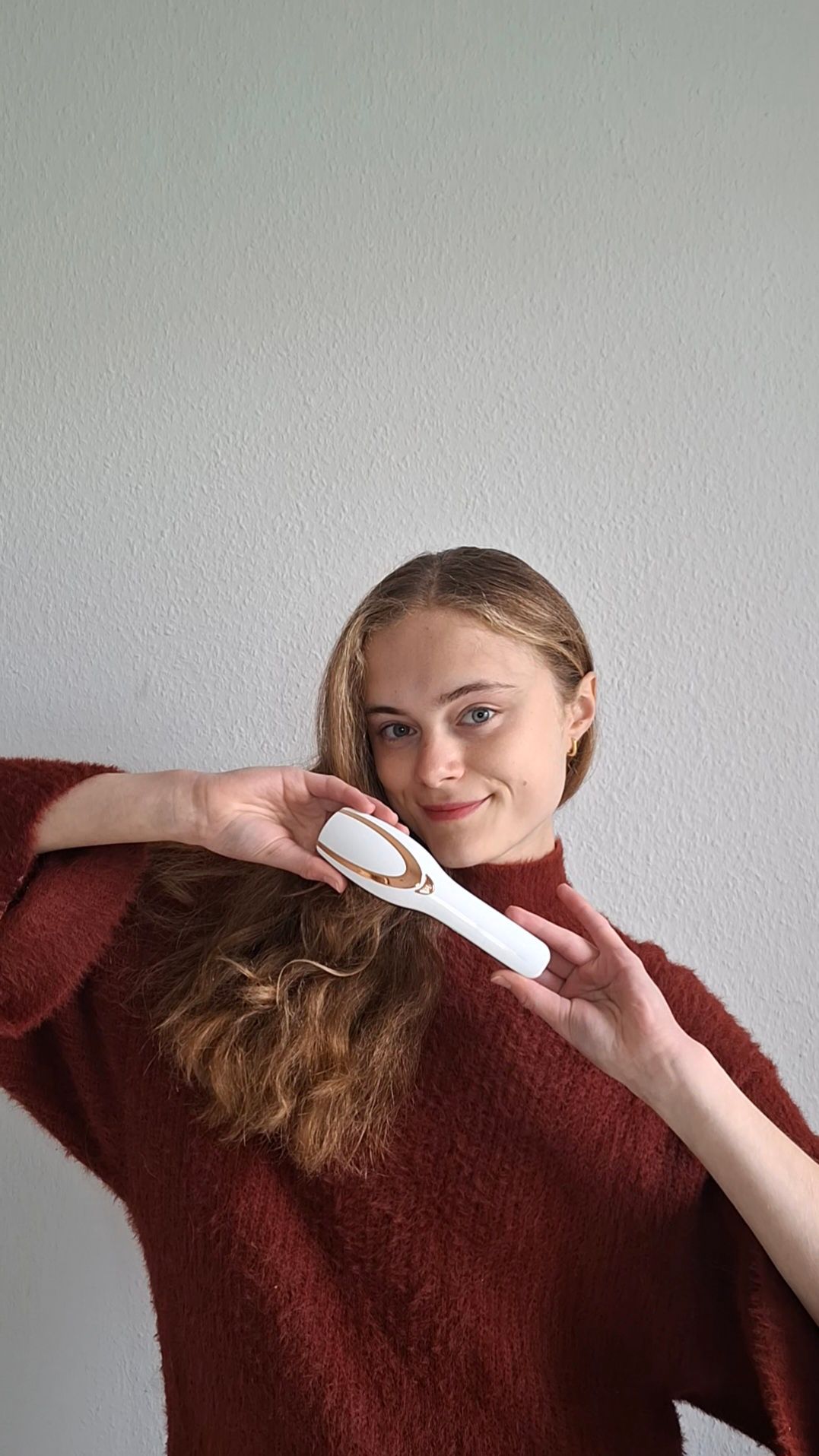 Apparecchio per spazzola per capelli bianco e oro. Una donna tiene l'apparecchio davanti ai suoi capelli. L'apparecchio è di forma ovale.